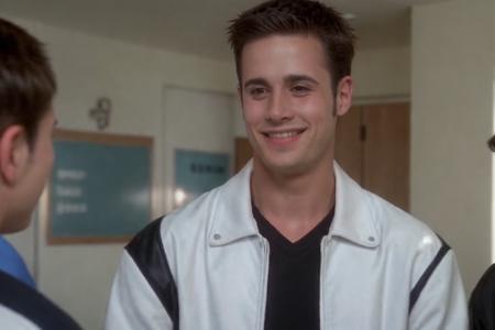 fpj, <lora:fpj-000002:1> a man in a black and white jacket walking in a high school, varsity jacket, (grin:0.7)