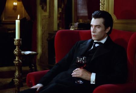 cinematic film still close-up of a vampire man with (pale skin:1.1) in a dark suit, sitting on a red armchair in a victorian living room, holding a glass of red wine, warm candle light at night, <lora:h4mm3r:0.8>