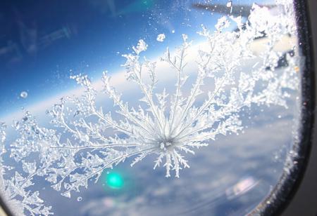 JNANX,luminous white silhouette,cyan glow,emerald highlights,flickering outline,dreamlike movement,
"A close-up view from an airplane window reveals intricate ice crystals forming on the outer pane. The blue sky and a portion of the aircraft's wing are visible in the background, distorted slightly by the frosty accumulation. Numerous delicate, feathery ice patterns spread across the window, with a denser, more concentrated cluster at the bottom center, almost appearing to grow upwards. Sunlight reflects off the icy surface, creating subtle glints. The overall impression is one of cold beauty, showcasing the unique atmospheric conditions encountered at high altitudes. The textures of the ice are varied, from fine dust-like particles to more defined, branching structures, suggesting a dynamic freezing process. The window itself has some minor smudges or imperfections, adding to the authenticity of the aerial perspective."