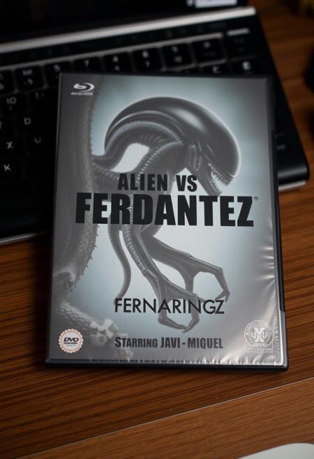 This is a photograph of DVD case with a desk background. The case features an alien and a xenomorph as in alien vs predator movie and a prominent black bold text "Alien VS Fernandez", Below is a bullet list of features: "Starring", "Javi" and "Miguel".