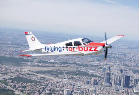 small plane is flying over the city, airplane banner attached to the plane, the inscription on the banner "flying for buzz"