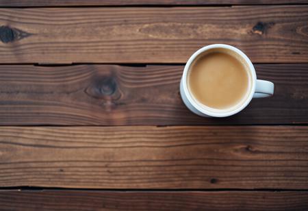 A view from the top of a wooden table with a coffee mug, classic stock photo, chill vibe, latte cafe on a classic wooden kitchen table. Empty table except the coffee mug. Coffee mug on the far right. Clean mug with fresh coffee, light foam on coffee.