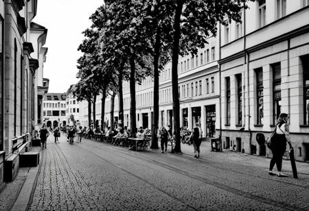 monochrome, instagram photo, a street in leipzig where i can see the westwerk on the right side. it's a summery atmosphere, in the afternoon at 16:00 and there are many people walking around on the street.