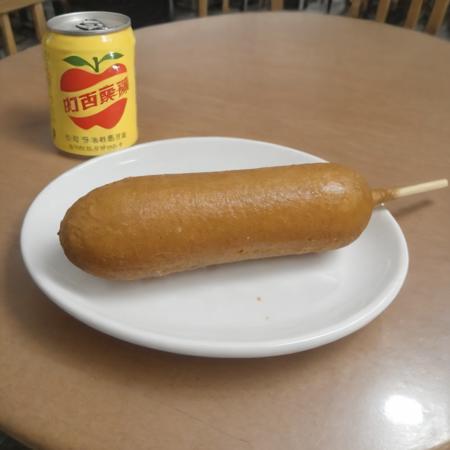 A photorealistic image of a delicious 9hotdog placed on a plate in a restaurant setting. The 9hotdog should be golden brown, with a crispy exterior and a juicy interior visible at one end where it's bitten off. The plate can be white or a light color to contrast with the golden hue of the 9hotdog. There might be a small dish of mustard or ketchup on the side for dipping. The table should have a clean tablecloth, and the lighting should be warm, highlighting the appetizing look of the 9hotdog. The background can have subtle hints of a restaurant ambiance, like a glass of water or some cutlery, <lora:cornhotdog:0.65>, (bottle of soda),<lora:applesoda:0.75>