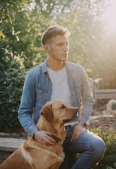 cinematic film still fashion photography portrait of 1man with dog as companion, grainy, headshot, sunlight , Fine Art & Beauty Photography – ,,light diffraction in frame, dreamy,hazy look.  Helios 44-2 lens mounted on a Praktica MTL 5B Helios 44M-4 lens, 58mm f/2,   in a garden.