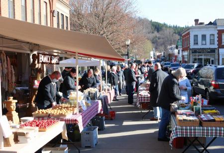 small town Saturday market day, sunny, northerly, crisp, tables, booths, crafts, homemade food, carvings, buyers, sellers, colorful, chocolate sop, bakery, parked cars, produce, berries, pottery, wool weaving, hot dog grilling, bookstore, bank building, tea room