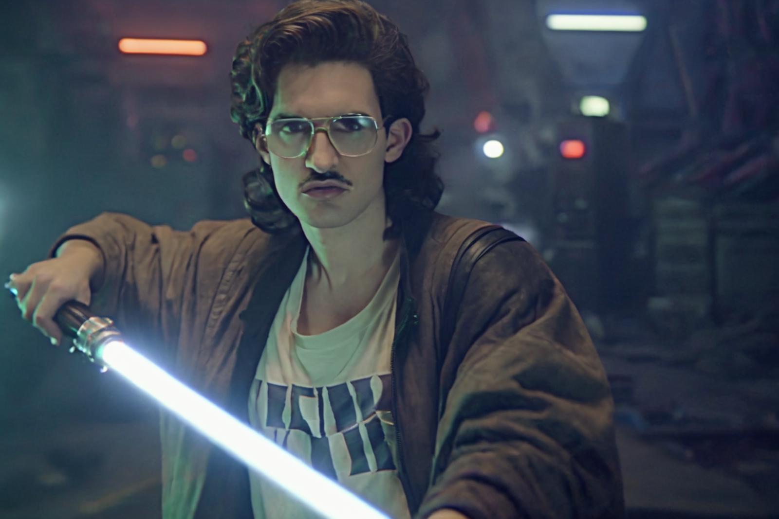 Man with a mustache and glasses holding a blue light saber.
