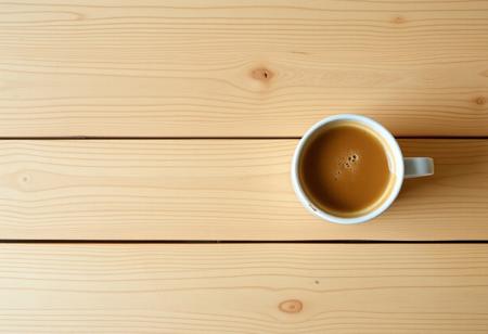 A view from the top of a wooden table with a coffee mug, classic stock photo, chill vibe, latte cafe on a classic wooden kitchen table. Empty table except the coffee mug. Coffee mug on the far right. Clean mug with fresh coffee, light foam on coffee. No space between plank, glued plank without gaps. Light coloured wood. Coffee mug should only take 1/16 of the image. view from far above
