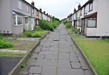A DLSR photo of a post apocalytic version of an average street of semi detached houses for normal people ,overcast day. windowless homes on both sides of the street.  The houses were painted mostly white or beige , or unpainted, now they are ruins, some have smoke damage or ar completely burnt.In front of the houses there are small gardens/driveways with low walls/hedging.The road is made of cracked concrete slabs sealed with tar along the edges. There are foothpaths on both sides. streetlights are broken unlit. glass on fragments the ground/road. parked against the foothpath and in driveways are affordable cars that are used, dirty, broken glass, open bonet, burnt out, dusty. Toyota, Hyundai, 
family, ordinary ,mundane,detailed , lived in, mediocre, realistic, messy, routine, humdrum, dull, boring, tedious, monotonous ,boring , ruined , affordable, bourgeois, working , working class, lower class, poverty, middle class, poor, real life, median, mortgage, consumerism, economic decline, debt, cracked glass, uninsured, run down, making do, modern, used, home, smoke damage, gonzo , potholes, abandoned, council, frugal,very good, honest , resourceful 
IKEA, LIDL, Tesco, Aldi, discount, mass produced , overgrown plants, clear text.
photorealistic, outdoors
consistent broken windows. end of time
post apocalpytic, smashed windows,scorch marks, rubbish in the street. 28 days later, Children Of Men