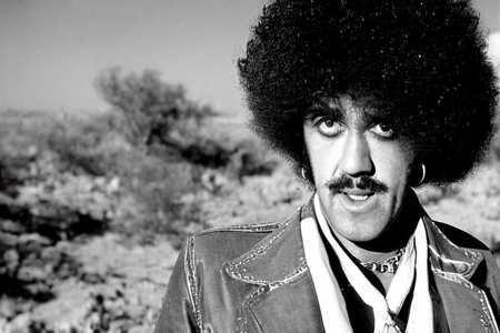 color photograph, ThinLizzy, TLPhil is 1boy  with a big afro dressed as cowboy, west texas desert,  detailed glossy eyes looking at viewer, visible skin pores,  highres, dof<lora:TLPhil:1>