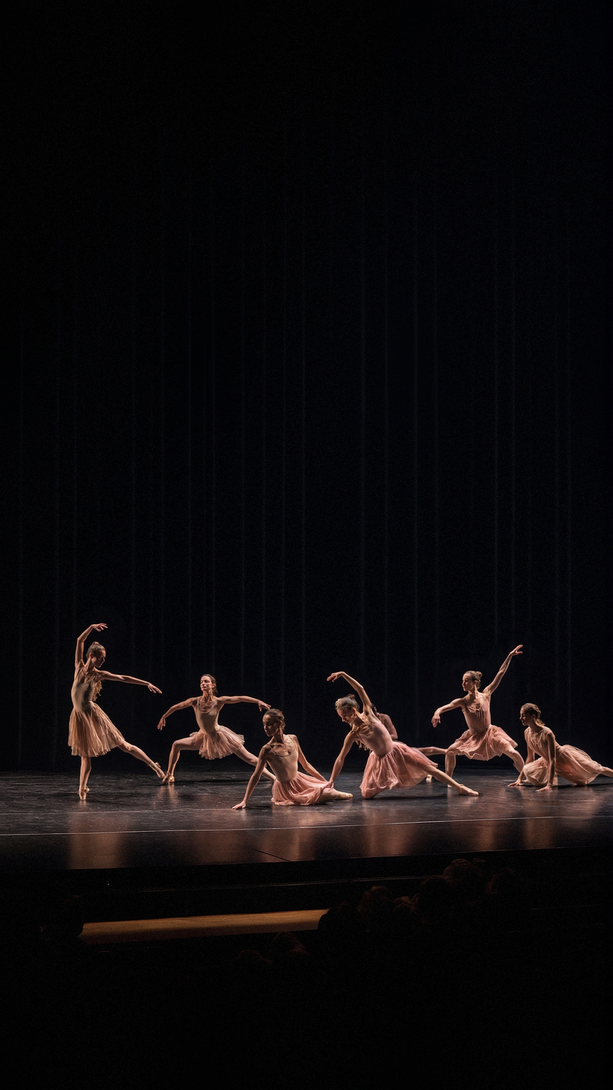 A group of dancers performing on stage in a darkened auditorium.