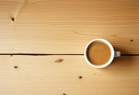 A view from the top of a wooden table with a coffee mug, classic stock photo, chill vibe, latte cafe on a classic wooden kitchen table. Empty table except the coffee mug. Coffee mug on the far right. Clean mug with fresh coffee, light foam on coffee. No space between plank, glued plank without gaps. Light coloured wood. Coffee mug should take 1/16 of the image. View from far above. Large table, small mug. Mug on top right corner. Tiny mug. Focus on table, not on mug
