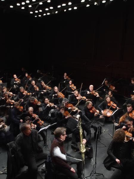 real, realistic, cinematic realism.
a full orchestra in a dark room, at least 20 members playing various impossible instruments like table legs and old boots and washboards.