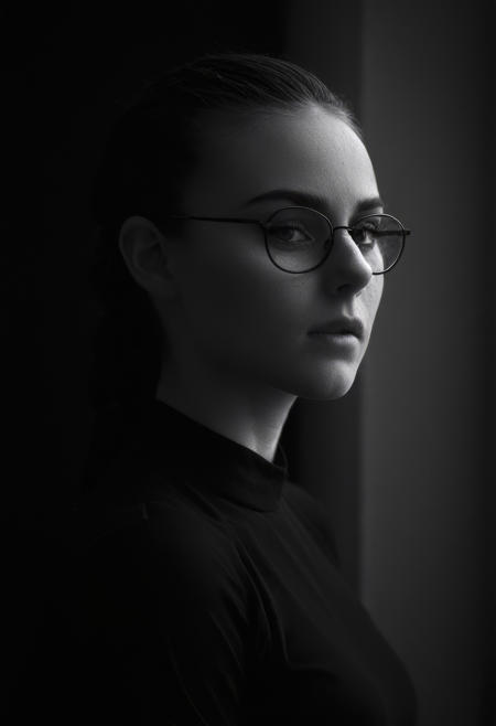 fine art portrait, masterpiece, infrared photography, black and white only, no colours used in image, close up dramatic face shot, full face and hair, dramatic side angled, beautiful young girl with prominent dimples and wearing glasses, creative bun hairstyle,
ultra detailed skin, perfect eyes, calm expression, 
realistic high resolution image, life like quality, cinematic scene with natural window lighting on partial face, background window in shallow depth of field, fine art portrait photography,
natural skin texture, fine pores, realistic skin, intricate skin details,, skin dentation, black and white, dark vignette around image,