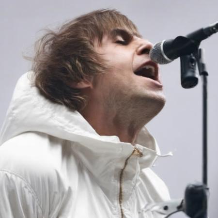 a photo of Li4mG4ll4gher, singing into a microphone, white parka, look moody, side facing, 4k, ultra detailed, masterpiece,  <lora:Li4mG4ll4gher:1.2>