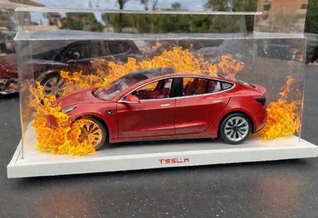 Hot Wheels toy car company have made a toy car version of a Tesla Model 3, The toy telsa model 3 car comes in a mini display unit/box. The car is exploding into fire and flames, white smoke fills the top of the display box, (realistic explosion from car), (realistic Flames bellow from the car windows inside the display unit),  (standing next to the car is a little palstic toy man, he holds both arms in the air, 