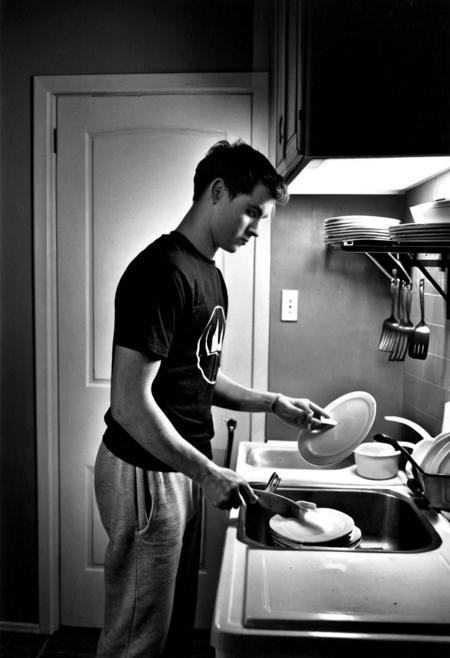 <lora:karsh_style_1-000008:1> monochrome karsh style, a young man in a t-shirt and sweat pants diligently doing the dishes, 2010, dim lighting, medium shot