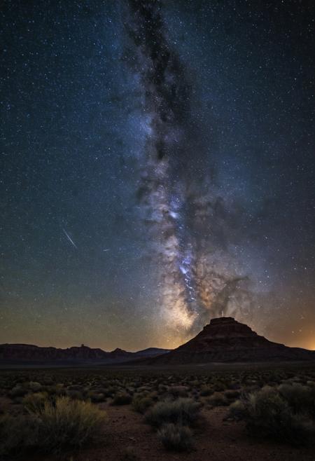 Capture the starry night sky over a desert landscape, with a Canon EOS R5 mirrorless camera and a 14mm f/2.8 lens, aperture f/2.8, shutter speed 20 sec, ISO 1600, to bring out the Milky Way and the distant stars.