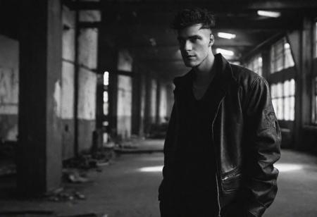 Lenar Karim photography style, tyson_dayley  , urban gritty location, posing in an industrial setting with steel beams, natural lighting, dramatic directional lighting, bold confident mood, black and white , Peter Lindbergh style