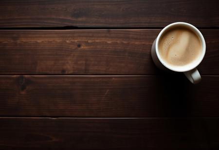 A view from the top of a wooden table with a coffee mug, classic stock photo, chill vibe, latte cafe on a classic wooden kitchen table. Empty table except the coffee mug. Coffee mug on the far right. Clean mug with fresh coffee, light foam on coffee. No space between plank, glued plank without gaps