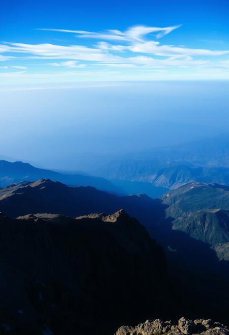 Immerse in a breathtakingly beautiful landscape: a vibrant blue-hued horizon stretches across the frame, fading into an atmospheric haze. Unusual dark colors, such as deep indigo and rich charcoal, punctuate the scene with dramatic flair. Cinematic lighting casts long shadows, emphasizing the fine details of the terrain. Film grain adds texture to the image, while superb composition guides the viewer's eye through the masterpiece. Maximum detail is achieved in every element, from the rugged terrain to the wispy clouds, creating an unparalleled level of visual mastery.