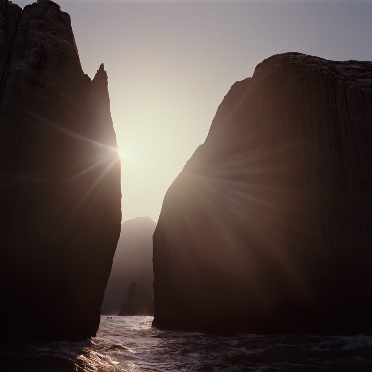 cinematic film still of  <lora:Ron Fricke style:1>
a large rock formation with a sun shining through it,outdoors,sky,water...