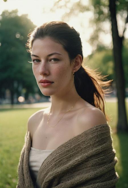 Grainy lowfi desaturated film photograph taken in a city park at dusk. Heavy Bokeh effect with focus on her green eyes, blurry background. A pretty young woman of northern Italian heritage wraps her brown cardigan around her bare shoulders. Goosebumps on a bare exposed shoulder. She wears the cardigan over a little summer sun dress and is chilly as the cool wind blows loose stands off her long black hair in her eyes. Tight ponytail. Fine Delicate thin gold chain necklace. She resembles Liv Tyler. The setting sun casts soft light into her eyes. Full soft cheeks and softer jawline, soft rounder oval face with the lightest freckles.