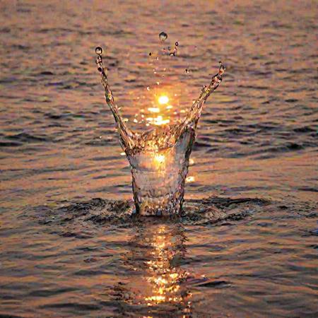 a crystal clear drop of water splashes into the sea at sunset, macro photography, melting reaction