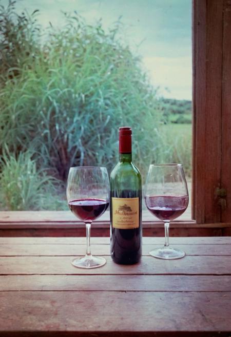 soaked_mundwasser, instagramphoto, a wooden table with a bottle of red wine and glas in a french restaurant, soft shadows, filmgrain