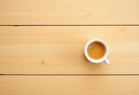 A view from the top of a wooden table with a coffee mug, classic stock photo, chill vibe, latte cafe on a classic wooden kitchen table. Empty table except the coffee mug. Coffee mug on the far right. Clean mug with fresh coffee, light foam on coffee. No space between plank, glued plank without gaps. Light coloured wood. Coffee mug should only take 1/16 of the image. View from far above. Large table, small mug