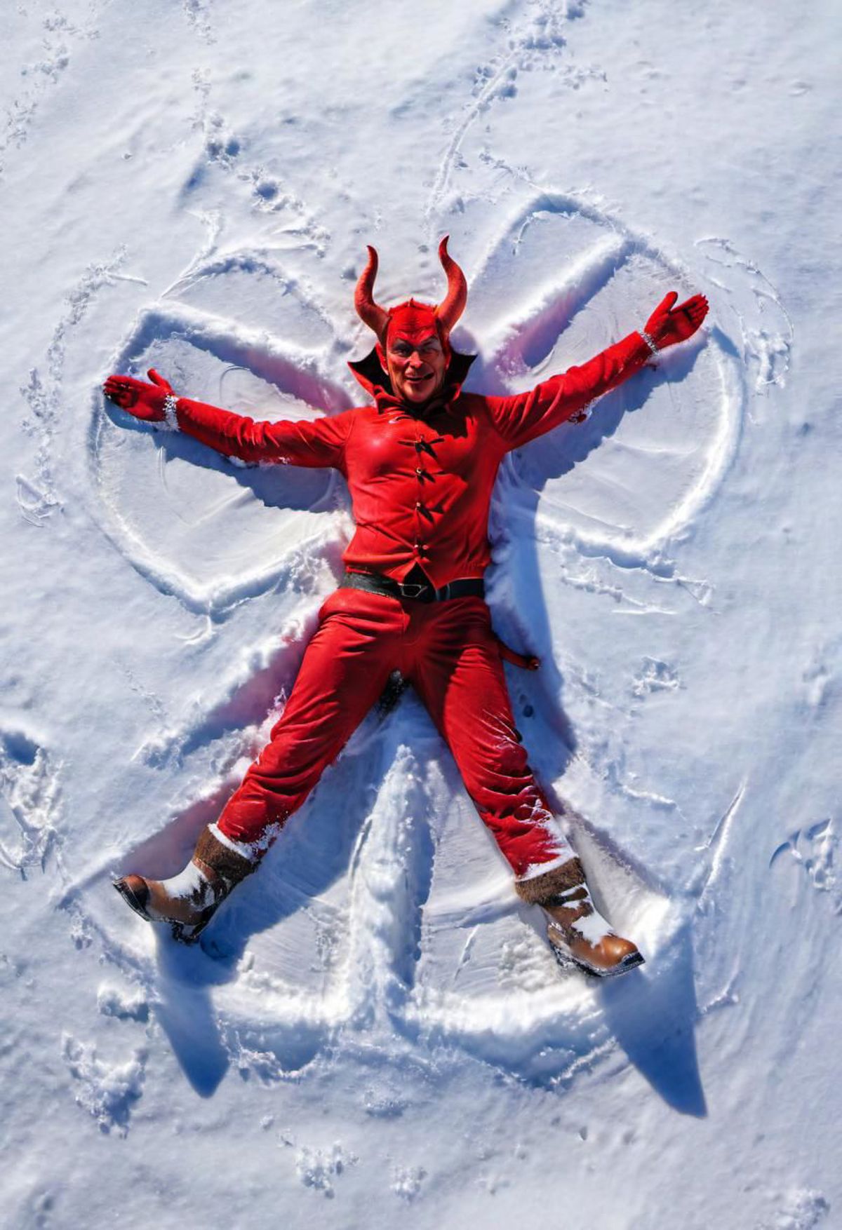A person in a red devil costume poses in a snowy field.