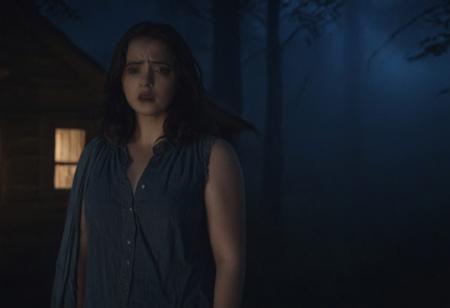 Cinematic frontal wide shot, landscape shot, dark night, full shot close up of dark haired woman standing and looking at someone offscreen, slight frown, scared expression on her face, backside of a large forest cottage with dim light, eerie, legion core, night lighting, muted color tones, dark blue and mahogany color tones, cinestill , fog, clouds, scary scenes,