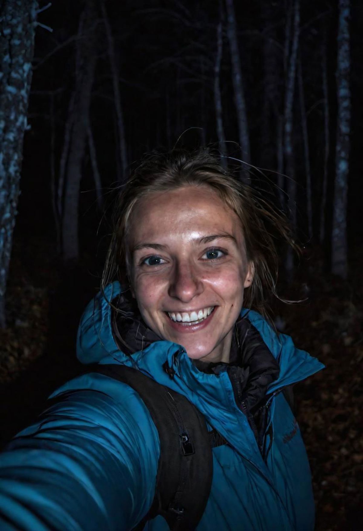 A woman in a blue jacket smiling in the woods.