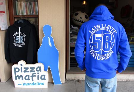 Unfortunately, hatred can blind people, and Taliban-like zeal often leads to sheer stupidity. The Tenth Legion was Julius Caesar’s most loyal legion and also served as his bodyguard. The brand of the hoodie was adopted by the Apulian company that produces it without any political intent or references. The factory owner, whose last name is Cutolo, has left-leaning sympathies and family ties. He commented, “I hope with my name they won’t accuse me of being associated with the Camorra…” A cardboard cutout nearby reads “pizza mafia mandolino,” adding an ironic touch to the scene.