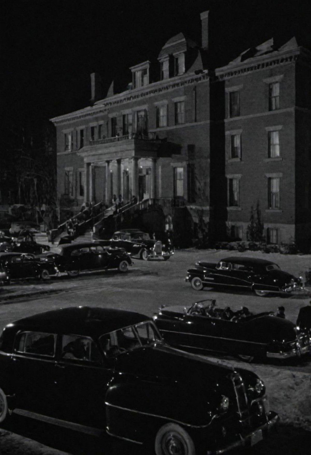 Vintage Black and White Photo of Classic Cars Parked in Front of a Large Building at Night