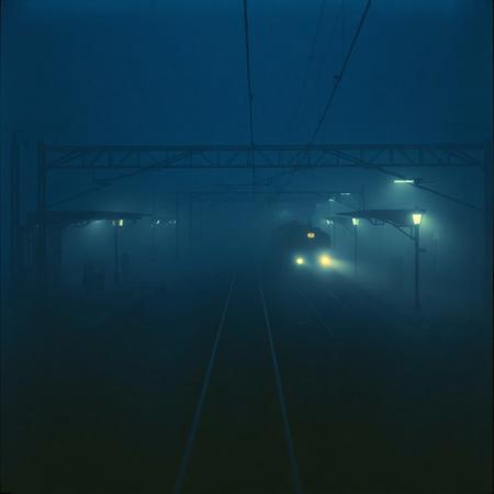 *"A still, hauntingly beautiful evening train station, bathed in deep blue hues and thick, slow-moving fog. The camera lingers motionless above the tracks, capturing the eerie stillness—only the faint glow of distant station lights piercing the mist. Suddenly, a slow, ghostly movement: a single train arrives silently, its headlights cutting through the fog like dim searchlights. The air shimmers with floating particles, and the scene feels frozen in time, yet alive with tension. No people, no loud sounds—just the quiet hum of machinery and the occasional creak of metal. Cinematic, 4K, 35mm film grain, muted colors, surreal and dreamlike."*