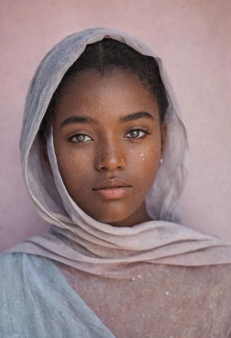 A portrait of a ethereal gorgeous 18-year-old black beauty , black women, with delicate freckles and soft, flawless black hair, her face partially obscured by sheer, flowing,The background is a smooth gradient of pastel colors, enhancing the dreamy, ethereal quality of the image. The color grading should emphasize the natural skin tones and subtle hues in her hair, with a gentle, glowing effect around her eyes blue eyes, black cotton fabric The focus is on her eyes, which are illuminated by a soft, hot on a Canon EOS R5 with a Canon RF 85mm f/1.2L lens by Marta Bevacqua.