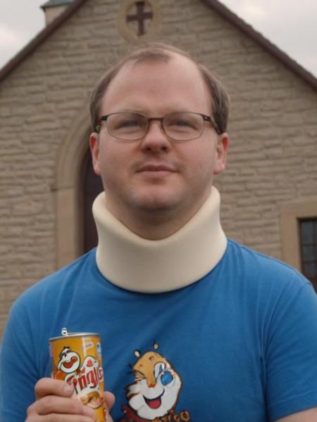 cinematic photo of  <lora:Tourettes_Guy:1> Tourettes Guy with a white neck brace and glasses in a blue shirt is holding a can of Pringles in front of a church, 35mm photograph, film, bokeh, professional, 4k, highly detailed