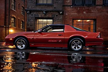 camaroirocz a red car parked on the side of a wet dark street at night next to a brick building, high resolution, high quality, intricate detail, very sharp <lora:hjcamaroirocz_v20:0.8>