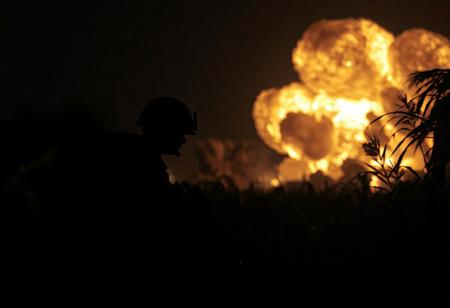 A dark night scene almost everything just silhouettes. A marine in a war zone in the asian jungle.
a huge realistic explosion in the background. no fire but flying dirt and plants. professional photography with a up to date DSLR. shallow depth of field.