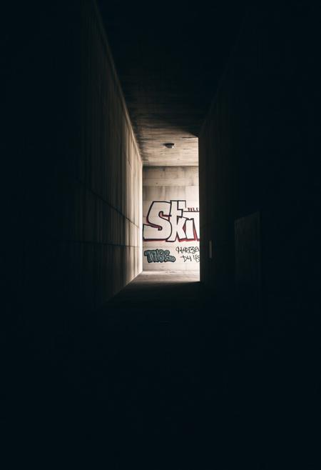 A dimly lit, monolithic concrete corridor where shadows cast hidden graffiti messages, blending the ephemeral nature of street art with controlled, meditative use of space..minimalist brutalist architecture meets provocative stencil street art, raw concrete and stone textures blending with high-contrast political imagery, atmospheric lighting with conceptual urban intervention, muted neutral tones with striking visual contrast, introspective space meets rebellious social critique