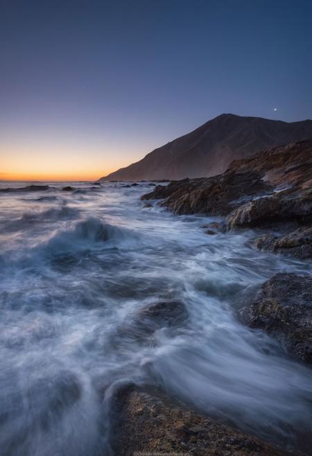 啎䥃佄䔀Capture the enchanting beauty of the transition from day to night, known as the blue hour, over a serene ocean with long exposure waves in the style of Michael Shainblum, using a Pentax K-1 Mark II camera with a Pentax D FA 24-70mm f/2.8 ED SDM WR lens. Position yourself to take advantage of the soft, diffused light of the twilight sky as it illuminates the ocean, casting long shadows and creating depth in your image. Experiment with different focal lengths to find the perfect composition, and use a tripod for stability during long exposures. Focus on the interplay of light and shadow, highlighting the rich textures and colors of the ocean under the twilight sky and long exposure waves. Utilize the cool tones of the blue hour to create a moody and atmospheric quality in your image. Post-process your image using techniques such as selective color grading and contrast adjustments to enhance the mood and atmosphere of the scene, creating a captivating and enigmatic photograph that embodies the essence of twilight transcendence with long exposure ocean waves in the style of Michael Shainblum.
