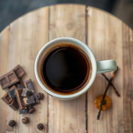 A cup of coffee on a wooden table, with hints of flavor Chocolate, Vanilla, Apricot, Pepper.