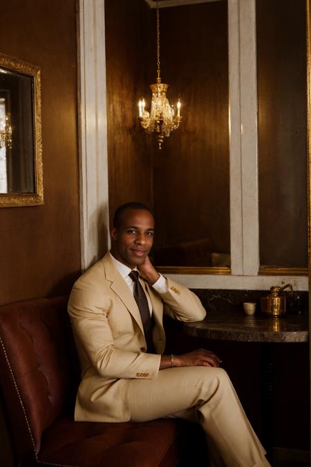 RAW Photo, photo of light-skinned African American man sc_chad3 <lora:sc_chad3-06:0.75> sitting introspectively in a booth in a Parisian-style cafe, contemplative smile, wearing tailored (tom ford suit) with ivory dress shirt and silk burgundy gucci tie with gold accents, deep mahogany walls, ornate gold-framed mirrors, ambient glow, dim interior, soft daylight filtering through lace curtains, aged wooden floor, brass espresso machine, porcelain, shadowed corners, serene atmosphere, nostalgic atmosphere, (vanity fair magazine), (photo by Sebastião Salgado)