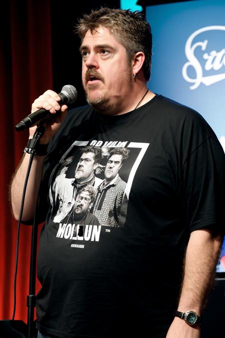 PhillJupitus clean-shaven holding a microphone wearing a graphic t-shirt, standup comedy <lora:rs-PhillJupitusLora-03:1>