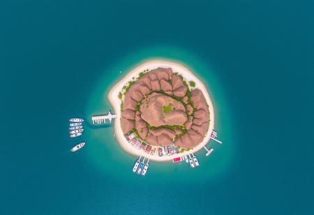 Yinyue Island is a tourist destination with a view of ships on the sea. The island has a radius of 2 kilometers and is crescent shaped with many mountains. It is surrounded by the sea and has attractions such as docks and villas.