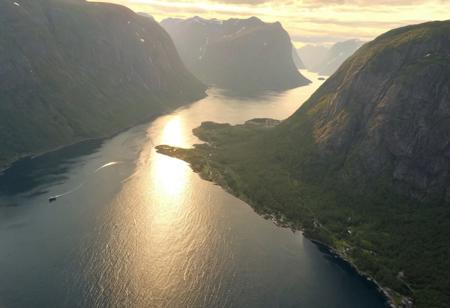 A from_above bird's-eye_view flying through a majestic fjord in Norway, summer, sunset