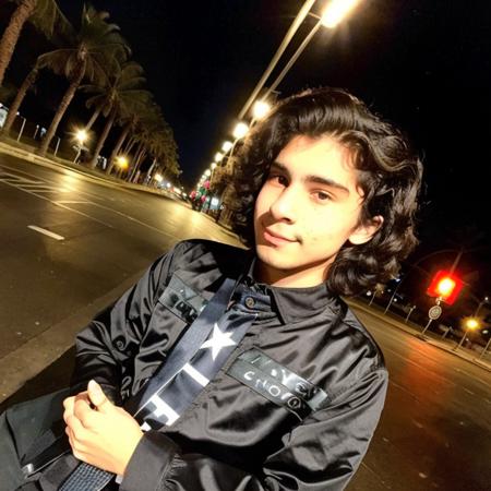 american shot photo of luis 19 years old, long cute hair, black clothes, night city street.