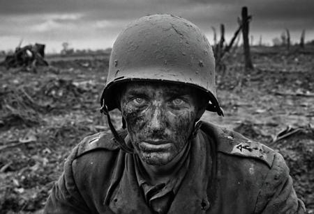 1 man, world war 2 soldier on the Eastern Front, (dying), (explosions), face in shadows, black and white, bright blue eyes, bloody face, bleeding out, exhausted, German Soldier, Stahlhelm helmet, muddy field, bleak landscape, last moments, <lora:Desolation:1.1>