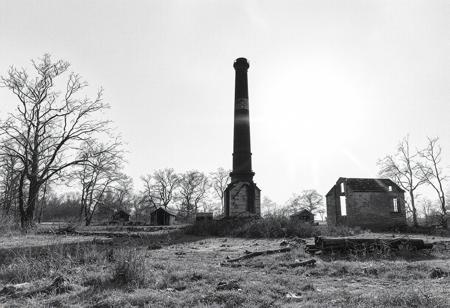 A lonely chimney of in the remains of former crematorium building. There are some ruined furnaces nearby. The background for the ruined, cold chimney is the bright daylight in the summer. No clouds, only hot August sun.
The picture is created in black and white watercolour technique, wherever possible black background is preferred.
The whole landscape is inspired by the atrocities of concentration camps and is the silent homage to the victims of the factories of death.